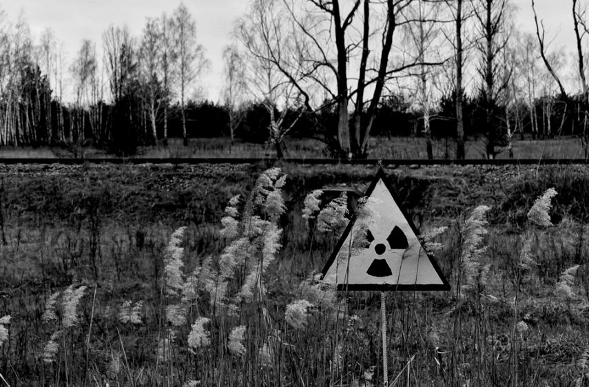 An empty, desolate landscape with a yellow and black nuclear warning sign foregrounded.